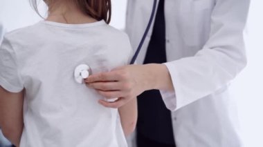 Doktor ve çocuk hasta klinikte. Beyaz önlüklü bir doktor steteskopla genç bir kızı muayene ediyor. İlaç, terapi konsepti.