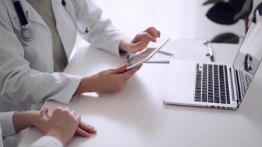 Doktor ve hasta klinikteki beyaz masada oturup test sonuçlarını tartışıyorlar. Bilinmeyen kadın doktor tablet bilgisayar kullanıyor. Tıp konsepti.