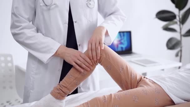 医生和病人在诊所里 穿白衣的整形外科医生检查一个小女孩的膝关节 物理治疗概念 — 图库视频影像