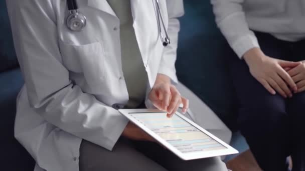 医師と患者はお互いに青いソファーに座っている タブレットコンピュータを使った未知の女性医師 医学コンセプト — ストック動画