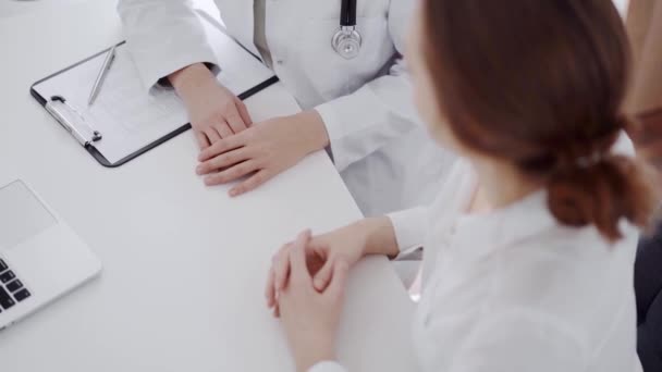 医師と患者は クリニックのホワイトデスクで お互いの近くで何かを話し合っている 女性医師が若い女性の声を聞き レコードを記録する 医学コンセプト — ストック動画