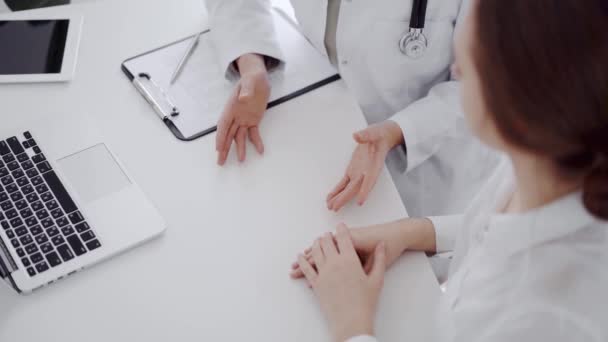 医師と患者は クリニックのホワイトデスクで お互いの近くで何かを話し合っている 女性医師が若い女性の声を聞き レコードを記録する 医学コンセプト — ストック動画