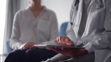 Doktor ve hasta mavi bir kanepede yan yana oturuyorlar. Bilinmeyen kadın doktor tablet bilgisayarı güvenle kullanıyor. Tıp konsepti.