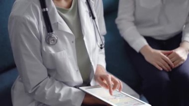 Doktor ve hasta mavi bir kanepede yan yana oturuyorlar. Bilinmeyen kadın doktor tablet bilgisayarı güvenle kullanıyor. Tıp konsepti.
