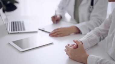 Doktor ve hasta klinikteki beyaz masada oturup test sonuçlarını tartışıyorlar. Bilinmeyen kadın doktor, genç bayanı dikkatle dinliyor. Tıp konsepti.