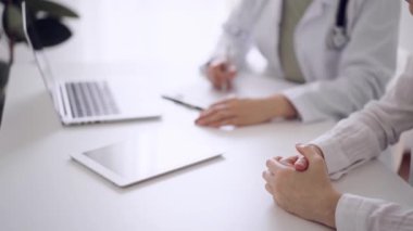 Doktor ve hasta klinikteki beyaz masada oturup test sonuçlarını tartışıyorlar. Bilinmeyen kadın doktor, genç bayanı dikkatle dinliyor. Tıp konsepti.