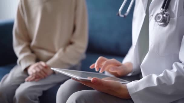 医師と患者はお互いに青いソファーに座っている タブレットコンピュータを使った未知の女性医師 医学コンセプト — ストック動画
