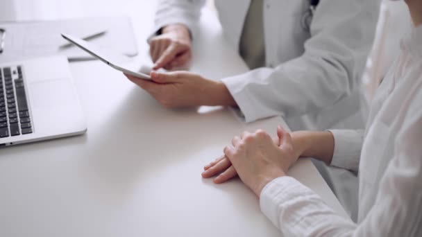 医師と患者は 診療所のホワイトデスクでお互いの近くでテスト結果について話し合っています タブレットコンピュータを使った未知の女性医師 医学コンセプト — ストック動画
