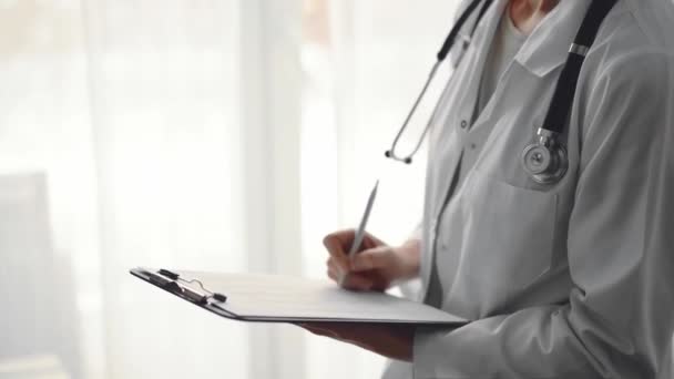 Doktor Kadın Klinikteki Panorama Penceresinin Yanında Dururken Tıbbî Kayıtları Doldurmak — Stok video