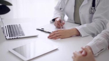 Doktor ve hasta klinikteki beyaz masada oturup test sonuçlarını tartışıyorlar. Bilinmeyen kadın doktor, genç bayanı dikkatle dinliyor. Tıp konsepti.