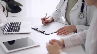 Doktor ve hasta klinikteki beyaz masada oturup test sonuçlarını tartışıyorlar. Bilinmeyen kadın doktor, genç bayanı dikkatle dinliyor. Tıp konsepti.