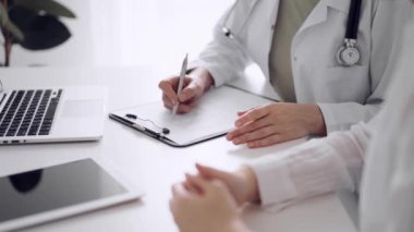 Doktor ve hasta klinikteki beyaz masada oturup test sonuçlarını tartışıyorlar. Bilinmeyen kadın doktor, genç bayanı dikkatle dinliyor. Tıp konsepti.