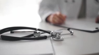 Steteskop yakınlarda yatarken, doktor kadın klinikteki ya da hastane ofisindeki beyaz masaya oturup notlar yazıyor. Tıp konsepti.
