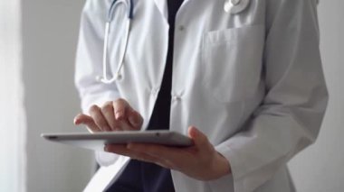 Doktor kadın klinikteki panorama penceresinin yanında dururken tablet bilgisayar kullanıyor. Tıptaki yetenekler.