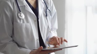 Doktor kadın klinikteki panorama penceresinin yanında dururken tablet bilgisayar kullanıyor. Tıptaki yetenekler.