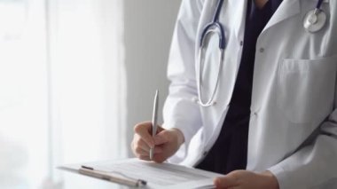 Doktor kadın, tıbbi notlar yazarken beyaz bir not panosu kullanıyor. Hastanenin panorama penceresinin yanında duran bilinmeyen bir doktor. İlaç..