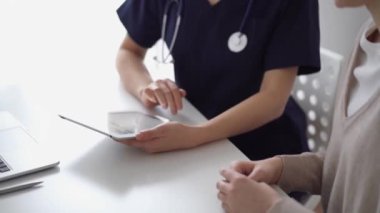 Doktor ve hasta klinikteki özel pencerenin yanındaki beyaz masada oturuyorlar. Bilinmeyen kadın doktor tıbbi kayıt formlarını doldurmak için tablet bilgisayar kullanıyor. Tıp konsepti.