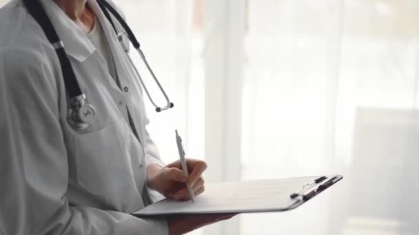 Ärztin Füllt Krankenakten Aus Während Sie Klemmbrett Hält Und Fenster — Stockvideo