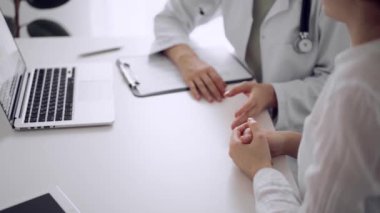 Doktor ve hasta klinikteki beyaz masada oturup bir şeyler tartışıyorlar. Kadın hekim bir kayıt formunu doldururken genç bir kadını dinliyor. Tıp konsepti.