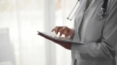 Doktor kadın klinikteki panorama penceresinin yanında dururken tablet bilgisayar kullanıyor. Tıp konsepti.