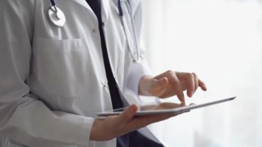 Doktor kadın klinikteki panorama penceresinin yanında dururken tablet bilgisayar kullanıyor. Tıptaki yetenekler.