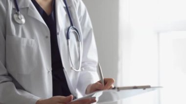 Doktor kadın, tıbbi notlar yazarken beyaz bir not panosu kullanıyor. Hastanenin panorama penceresinin yanında duran bilinmeyen bir doktor. İlaç..