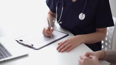 Doktor ve hasta klinikteki yetenek penceresinin yanındaki beyaz masada oturup test sonuçlarını tartışıyor. Bilinmeyen doktor tıbbi kayıt formlarını doldurmak için pano kullanıyor. Tıp konsepti.