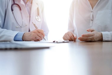 Doktor ve hasta klinikteki ahşap masada yan yana oturuyorlar. Kadın doktorlar kayıt formunu dolduruyorlar. Tıp konsepti.