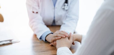 Doktor ve hasta klinikteki ahşap masada oturuyorlar. Kadın doktorların elleri güven veren kadınlarındır. Tıp konsepti.