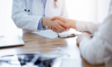 Doktor ve hasta klinikteki ahşap masanın üstünde el sıkışıyor. Tıp konsepti.