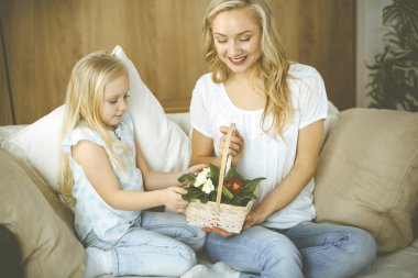 Anneler Günün kutlu olsun. Çocuk kızı annesini tebrik ediyor ve ona bir sepet bahar çiçeği ve kalp çizimi olan bir kartpostal veriyor. Aile ve çocukluk kavramları.