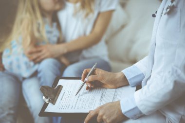 Doktor ve hasta. Pediyatrist, annesiyle birlikte küçük kızı muayene ederken pano kullanıyor. Sağlık muayenesinde hasta ve mutsuz bir çocuk. Tıp konsepti.