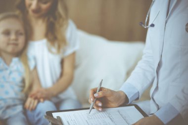 Doktor ve hasta. Pediyatrist, annesiyle birlikte küçük kızı muayene ederken pano kullanıyor. Sağlık muayenesinde hasta ve mutsuz bir çocuk. Tıp konsepti.