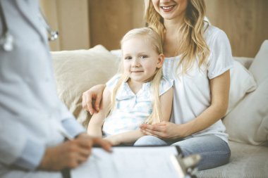 Doktor ve hasta. Pediyatrist, annesiyle birlikte küçük kızı muayene ederken pano kullanıyor. Sağlık muayenesinde mutlu beyaz çocuk. Tıp konsepti.