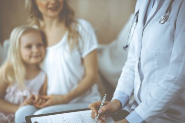 Doktor ve hasta. Pediyatrist, annesiyle birlikte küçük kızı muayene ederken pano kullanıyor. Sağlık muayenesinde mutlu beyaz çocuk. Tıp konsepti.