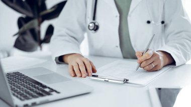 Bilinmeyen doktor kadın klinikteki ya da hastane ofisindeki masaya oturup notlar yazıyor. Kapat. Tıp konsepti.