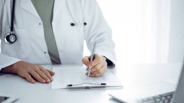 Bilinmeyen doktor kadın klinikteki ya da hastane ofisindeki masaya oturup notlar yazıyor. Kapat. Tıp konsepti.