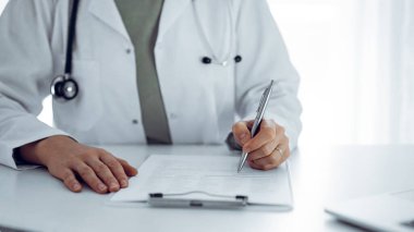 Bilinmeyen doktor kadın klinikteki ya da hastane ofisindeki masaya oturup notlar yazıyor. Kapat. Tıp konsepti.