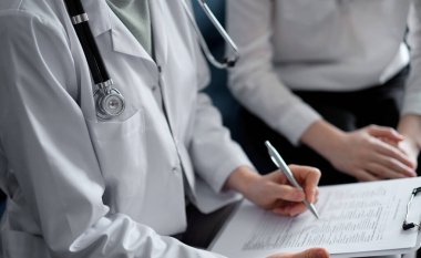 Doktor ve hasta klinikteki koltukta oturuyor. Kadın doktorların ellerinin ilaç geçmişi formunu doldurmasına odaklan, kapat. Tıp konsepti.