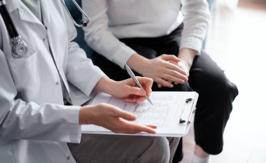 Doktor ve hasta klinikteki koltukta oturuyor. Kadın doktorların ellerinin ilaç geçmişi formunu doldurmasına odaklan, kapat. Tıp konsepti.