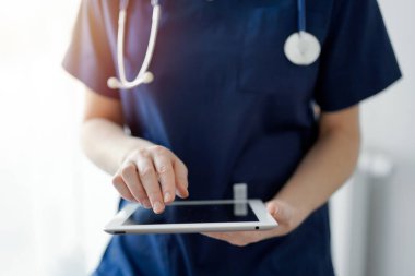 Doktor kadın panorama penceresinin yanında dururken tablet bilgisayar kullanıyor, kapatın. Doktor ya da cerrah iş başında. Tıp konsepti.