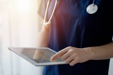 Doktor kadın panorama penceresinin yanında dururken tablet bilgisayar kullanıyor, kapatın. Doktor ya da cerrah iş başında. Tıp konsepti.