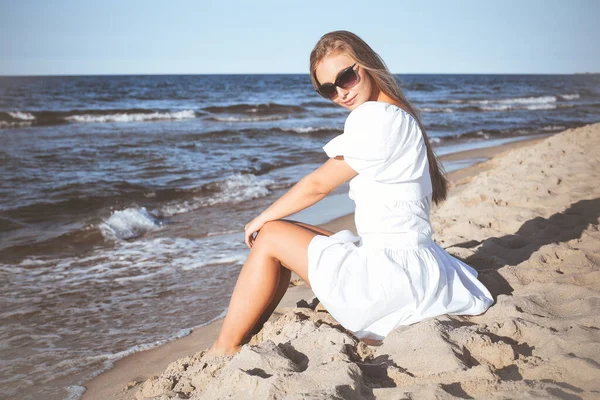 Šťastná Krásná Blondýna Žena Sedí Pláži Oceánu Bílých Letních Šatech — Stock fotografie