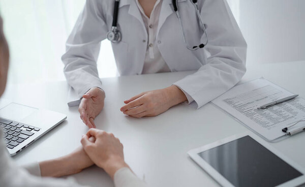Doctor and patient discussing current health questions while sitting at the desk in clinic office, closeup. Medicine and healthcare concept.