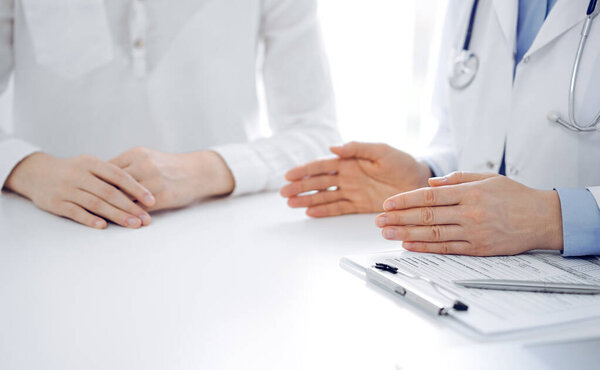 Врач и пациент обсуждают текущие вопросы здоровья, сидя рядом друг с другом за столом в клинике, только руки крупным планом. Концепция медицины.