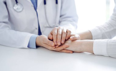 Doktor ve hasta klinikteki masada yan yana oturuyorlar. Kadın doktorlara odaklan. Kadına güven veren eller, sadece eller, yakın çekim. Tıp konsepti.