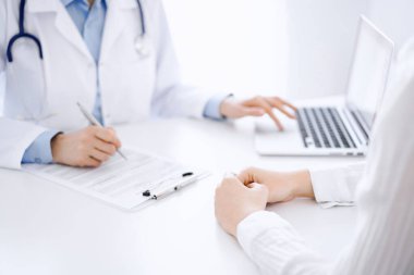 Doktor ve hasta bir şey tartışıyor ve klinikteki masada karşılıklı otururken dizüstü bilgisayar kullanıyorlar. Mükemmel tıbbi hizmet ve tıp konsepti.