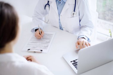 Doktor ve hasta bir şey tartışıyor ve klinikteki masada karşılıklı otururken dizüstü bilgisayar kullanıyorlar. Mükemmel tıbbi hizmet ve tıp konsepti.