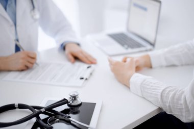 Arka planda karşılıklı oturan bir doktor ve hastanın önündeki tablet bilgisayarın üzerinde steteskop var. Tıp, sağlık hizmeti kavramı.