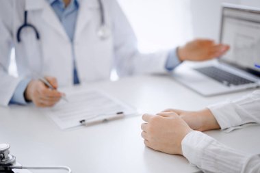 Doktor ve hasta klinikteki masada karşılıklı otururken tablet bilgisayar kullanıyorlar. Doktorun yanındaki kadın ellerine odaklan, yakın çekim. Tıp konsepti.